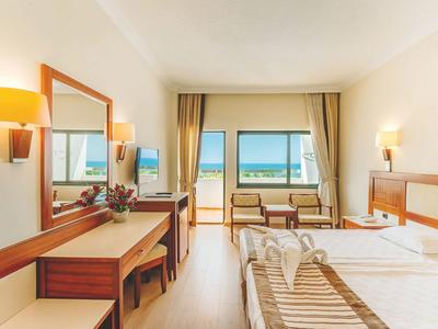 Chambre d'hôtel avec lit double, bureau, fauteuils et vue sur l'océan par la fenêtre.