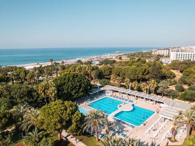 Complex avec une grande piscine extérieure entourée de palmiers près du littoral.