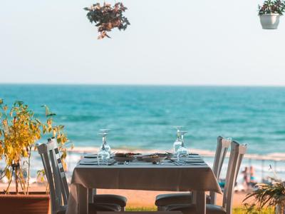 Een gedekte tafel met vier stoelen op een terras met uitzicht op de zee en hangende bloemen.