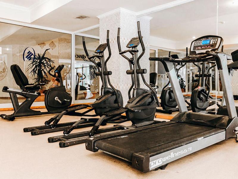 Salle de sport moderne avec tapis de course, elliptiques et vélos stationnaires dans une salle lumineuse.