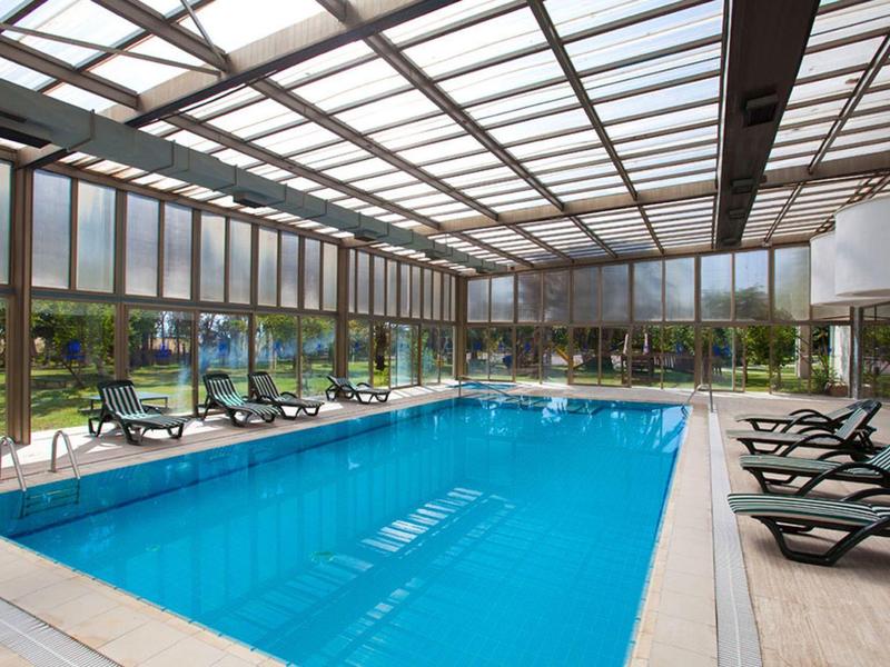 Piscine intérieure avec chaises longues et grandes fenêtres en verre donnant sur un jardin.