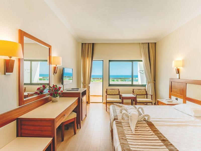 Chambre d'hôtel avec lit double, bureau, fauteuils et vue sur l'océan par la fenêtre.