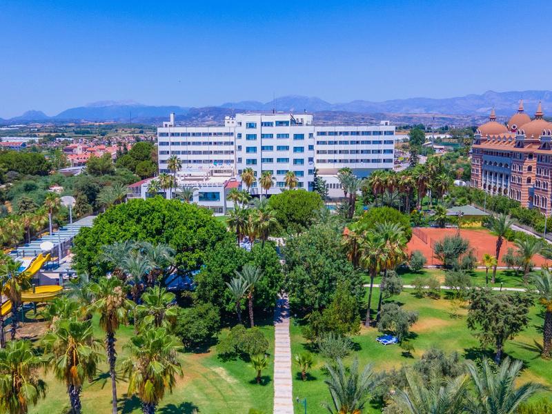 Grand hôtel entouré de verdure avec un ciel bleu clair en arrière-plan.