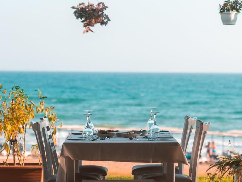 Table à manger en bord de mer pour deux sous une terrasse ombragée avec des plantes suspendues.