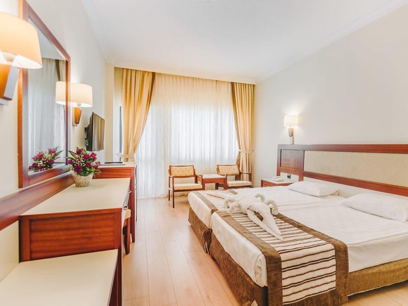 Chambre d'hôtel lumineuse avec deux lits, une coiffeuse et un coin salon près de la fenêtre.