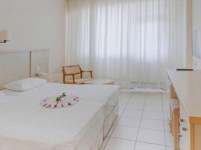 Lichte hotelkamer met groot bed, wit beddengoed, bureau, stoel en transparante gordijnen.