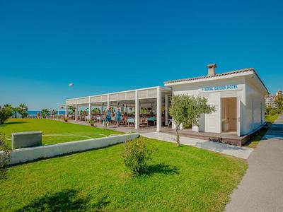 Éénlaagse hotel met zitplaatsen buiten en groen gazon onder een heldere blauwe hemel