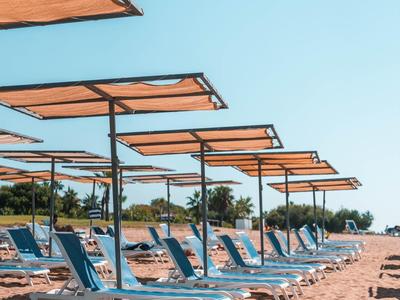 Strand met rijen blauwe ligstoelen en oranje zonneschermen op een zonnige dag.