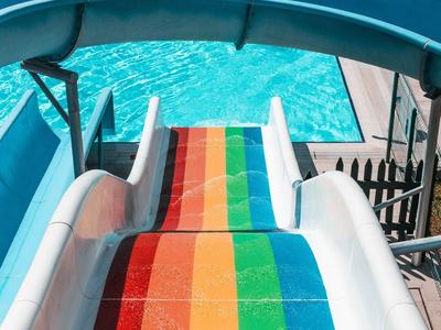 Kleurrijke glijbaan die uitkomt in een zwembad met ligstoelen in de buurt.