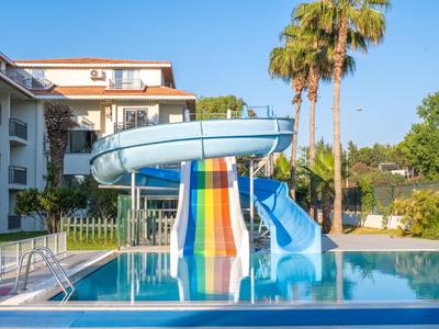 Piscina con scivolo d'acqua colorato in un hotel con palme e cielo limpido sullo sfondo.