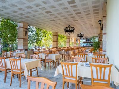 Buiten eetgedeelte met houten stoelen en tafels bedekt met witte tafelkleden onder een plafond.