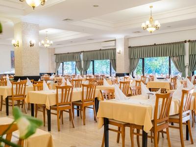 Ruime hoteldiner met houten stoelen en tafels met witte tafelkleden en glaswerk.