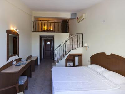 Minimalistische hotelkamer met wit bed, houten bureau, spiegel en trap naar een loft.