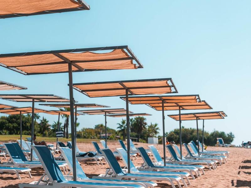 Strand met rijen blauwe ligstoelen en oranje zonneschermen op een zonnige dag.