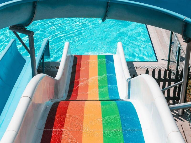 Kleurrijke glijbaan die uitkomt in een zwembad met ligstoelen in de buurt.