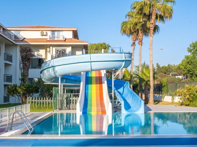 Buitenzwembad met kleurrijke glijbaan en palmbomen bij een zonnig resort.