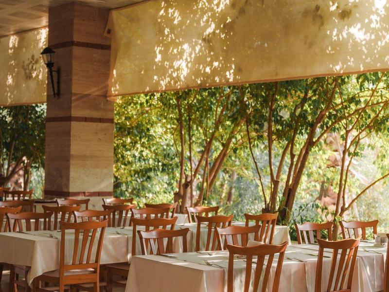Buitenterras met houten stoelen en witte tafelkleden onder een beschutte pergola.