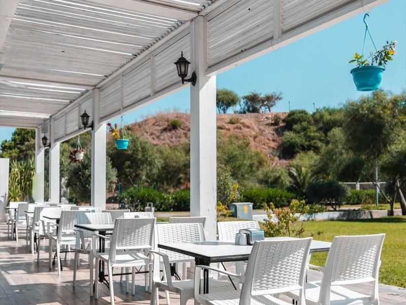 Buitenterras van hotel met witte stoelen en tafels onder een gestreept dak in een zonnige tuin.