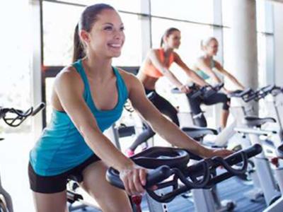 Mujeres haciendo ejercicio en bicicletas estáticas en un gimnasio iluminado.