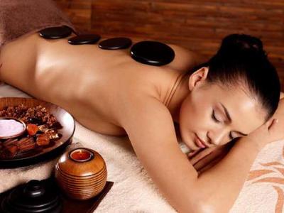 Frau liegt entspannt mit heißen Steinen auf dem Rücken in warmem, ruhigem Spa-Ambiente.