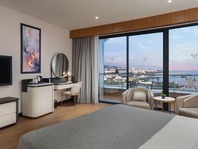Helles Hotelzimmer mit großem Fenster und Blick auf Hafen und Stadt.
