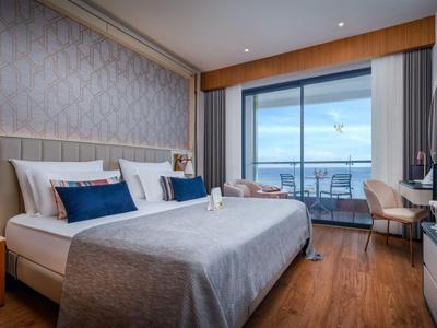 Modernes Hotelzimmer mit Doppelbett, Schreibtisch und Meerblick durch große Fenster.