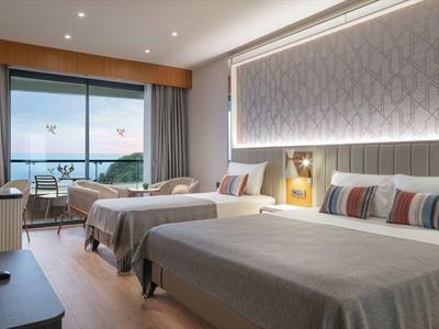 Modernes Hotelzimmer mit zwei Betten, großem Fenster und Sitzecke mit Blick auf Wasser.
