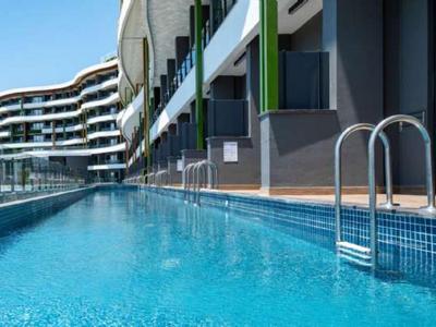 Moderner Außenpool mit klarem Wasser, blauen Fliesen und weißen Geländern an einer Wohnanlage.