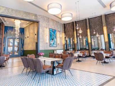 Geräumiges, elegantes Café mit hohen Decken, großen Fenstern, hellen Wänden und modernen Loungemöbeln.