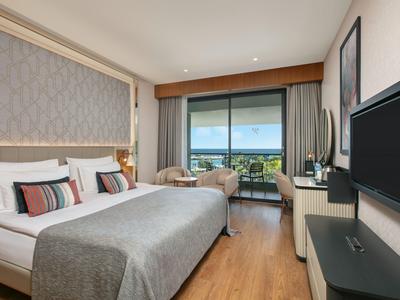 Modernes Hotelzimmer mit Doppelbett, Balkon und Meerblick bei Tageslicht.