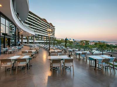Terrasse eines Hotels mit leeren Tischen und Stühlen, Blick auf das Meer und Sonnenuntergang.