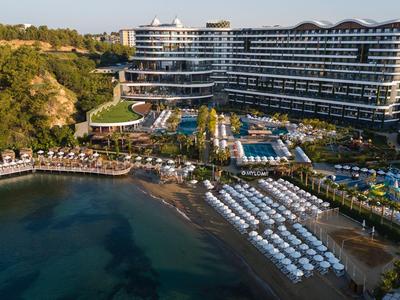 Großes Hotel mit Pools und Strandliegen an einer Küste mit klarem Wasser.