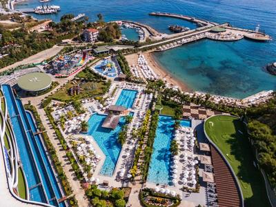 Luftaufnahme eines Resorts mit Pools, Liegestühlen und einem Strand an einer blauen Küste.