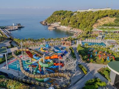 Wasserpark mit bunten Rutschen am Meer, umgeben von grünen Hügeln und blauer See.