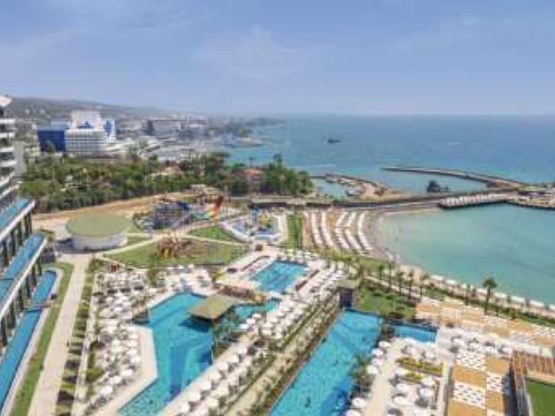 Großes Hotel mit blauen Pools, Liegestühlen, Palmen und Blick auf das blaue Meer und den Himmel.