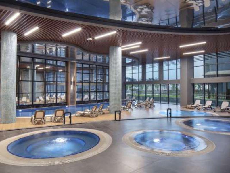 Modernes Hallenbad mit großem Fenster, zwei runden Whirlpools und Lounge-Stühlen am Rand.