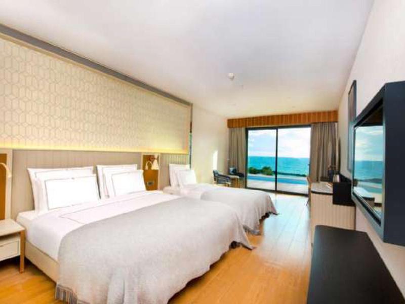 Modernes Hotelzimmer mit zwei großen Betten, Holzboden und Blick auf das Meer durch eine Glasfront.