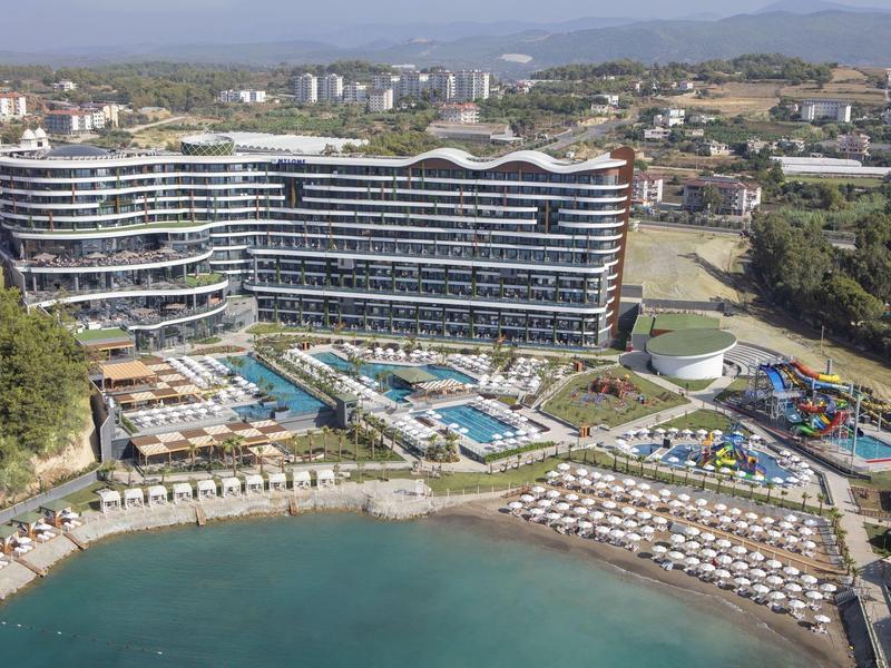 Großes Hotel mit mehreren Pools und Wasserrutschen am Ufer eines ruhigen Meeres.