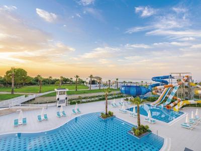 Duży basen na zewnątrz z zjeżdżalniami wodnymi i leżakami o zachodzie słońca.