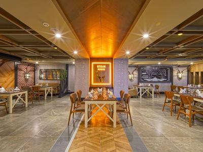 Przestronna restauracja z drewnianą podłogą, nowoczesnymi kolorowymi wzorami na ścianach i stolikami z wygodnymi krzesłami.