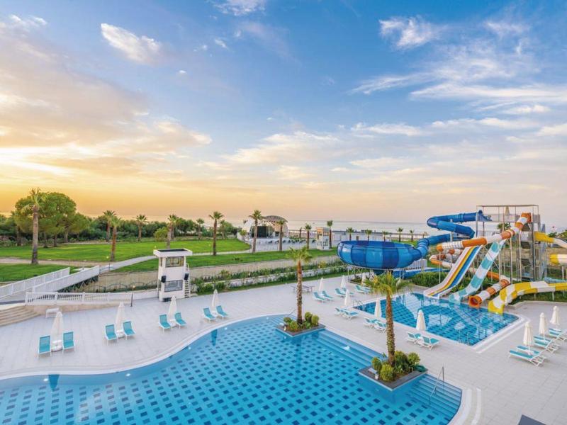 Duży basen na zewnątrz z zjeżdżalniami wodnymi i leżakami o zachodzie słońca.
