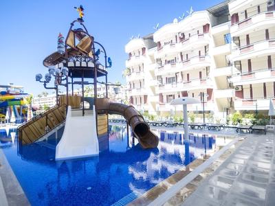 Área de juegos acuáticos para niños con toboganes junto a un edificio de apartamentos bajo sol.