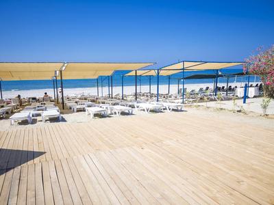 Área exterior vacía con terraza de madera y sombrillas en una playa soleada bajo cielo azul.