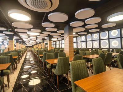 Comedor moderno con sillas verdes, mesas de madera y diseño de luces redondas en el techo.