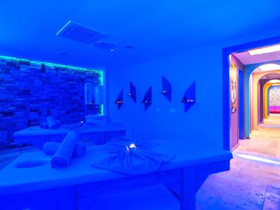 Área de spa moderna con camilla de masaje iluminada en azul y pasillo adyacente con luces coloridas.