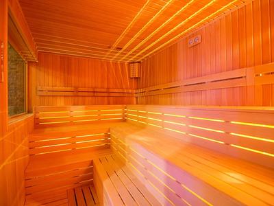 Sauna de madera clara con bancos escalonados y luz indirecta en las paredes.