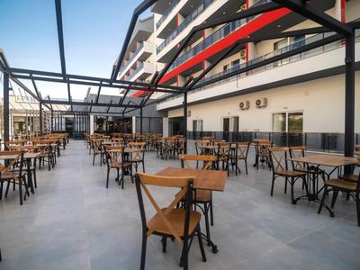 Gran terraza con mesas y sillas de madera frente a un edificio de hotel con balcones.