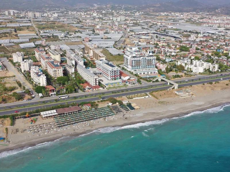 Vista aérea de una ciudad costera con playa, paseo marítimo y agua azul clara.