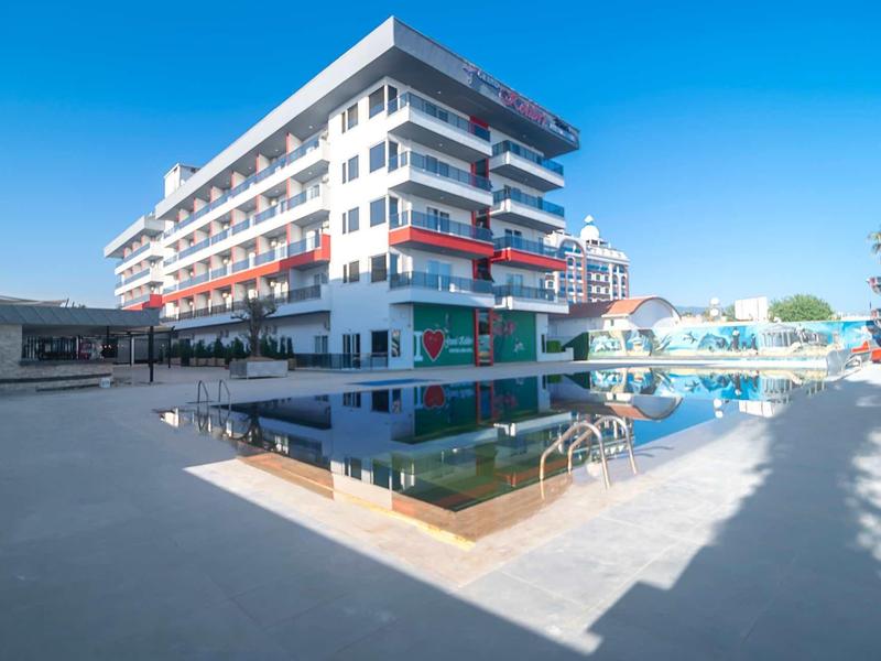 Edificio de hotel de varios pisos con balcón y piscina bajo un cielo azul.