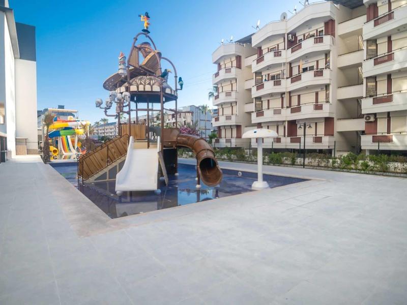 Área de juegos moderna con tobogán y túnel en un complejo hotelero bajo cielo despejado.